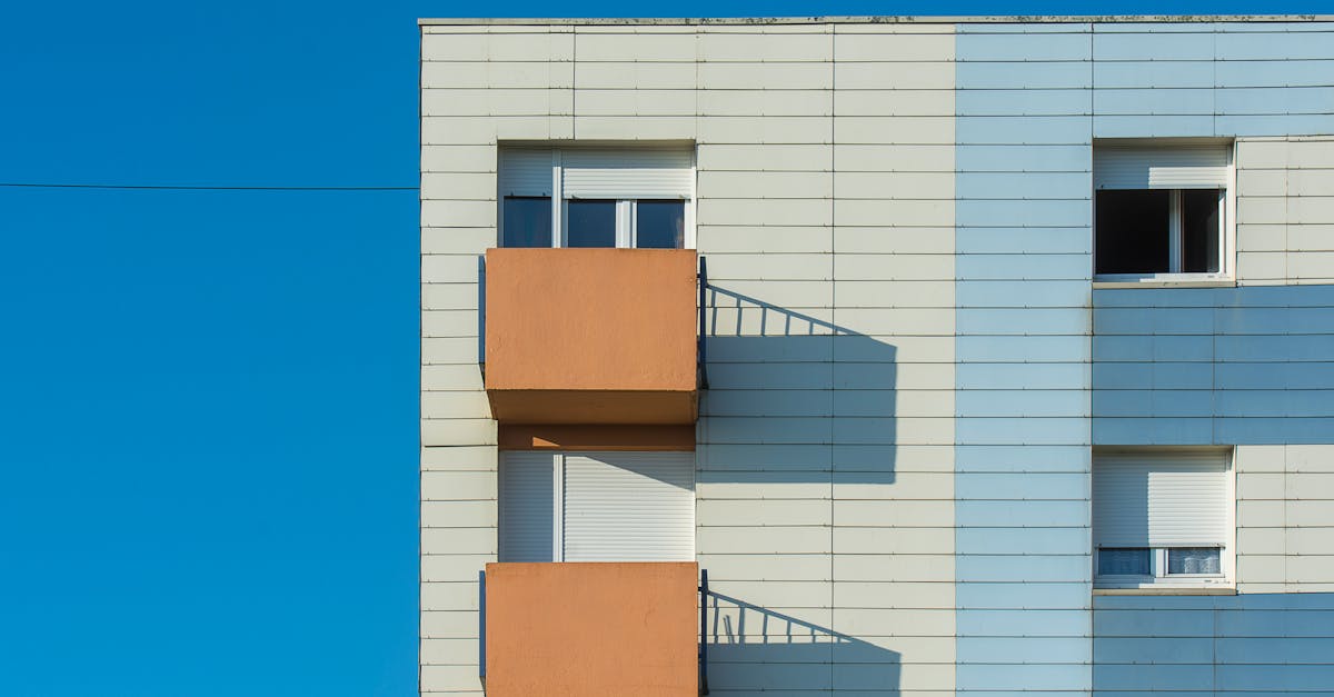 Services White modern apartment building with balconies casting distinct shadows under a clear blue sky.